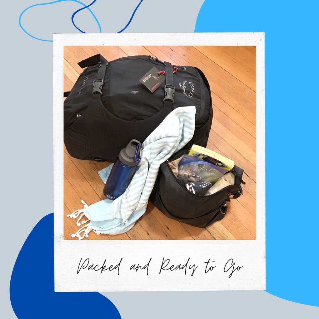 black carry-on backpack full, behind a water bottle, and Turkish towel, and an open purse containing a book and two bags