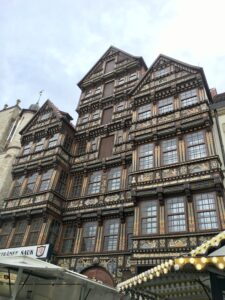 Brown, wooden six story building with many windows and a facade covered in ornate paintings and gold text