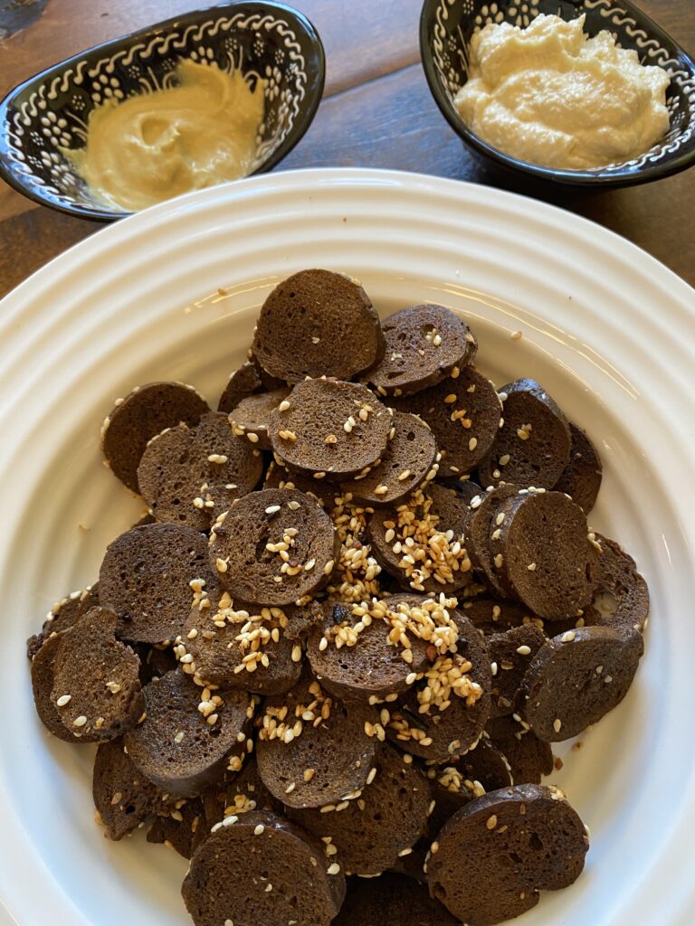 Pumpernickel rye chips in a bowl with two dip bowls behind them