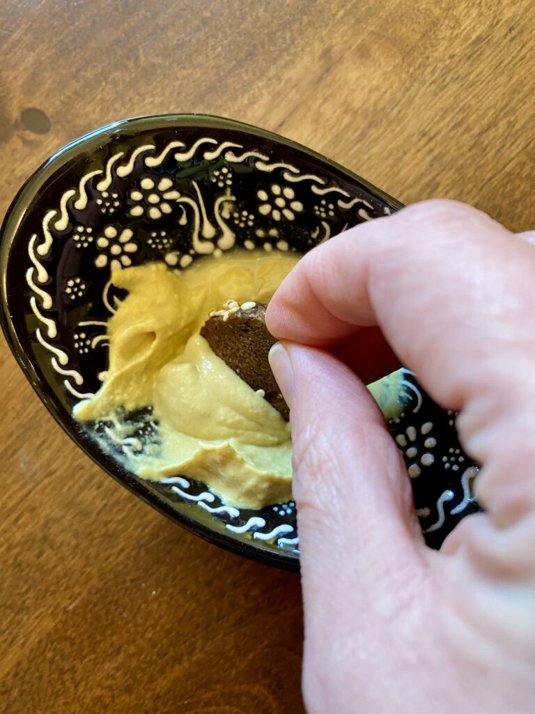 Mustard dip in a bowl with a hand dipping a pumpernickel rye chip